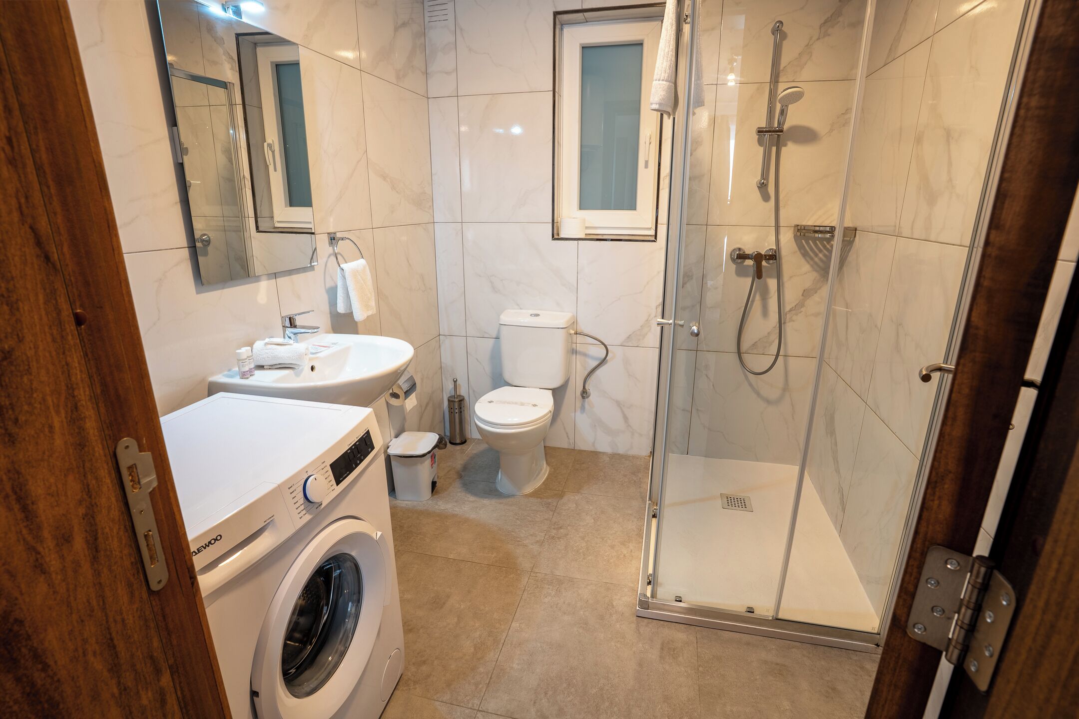 A bathroom with a washing machine, toilet, sink, and glass-enclosed shower.