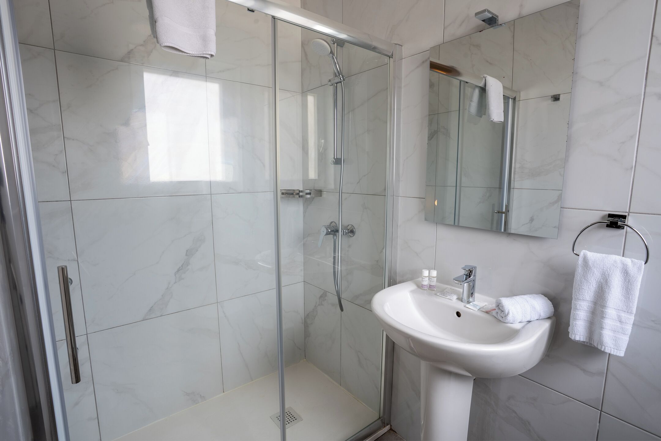 Een moderne badkamer met een glazen douchecabine, een witte wastafel en een spiegel.