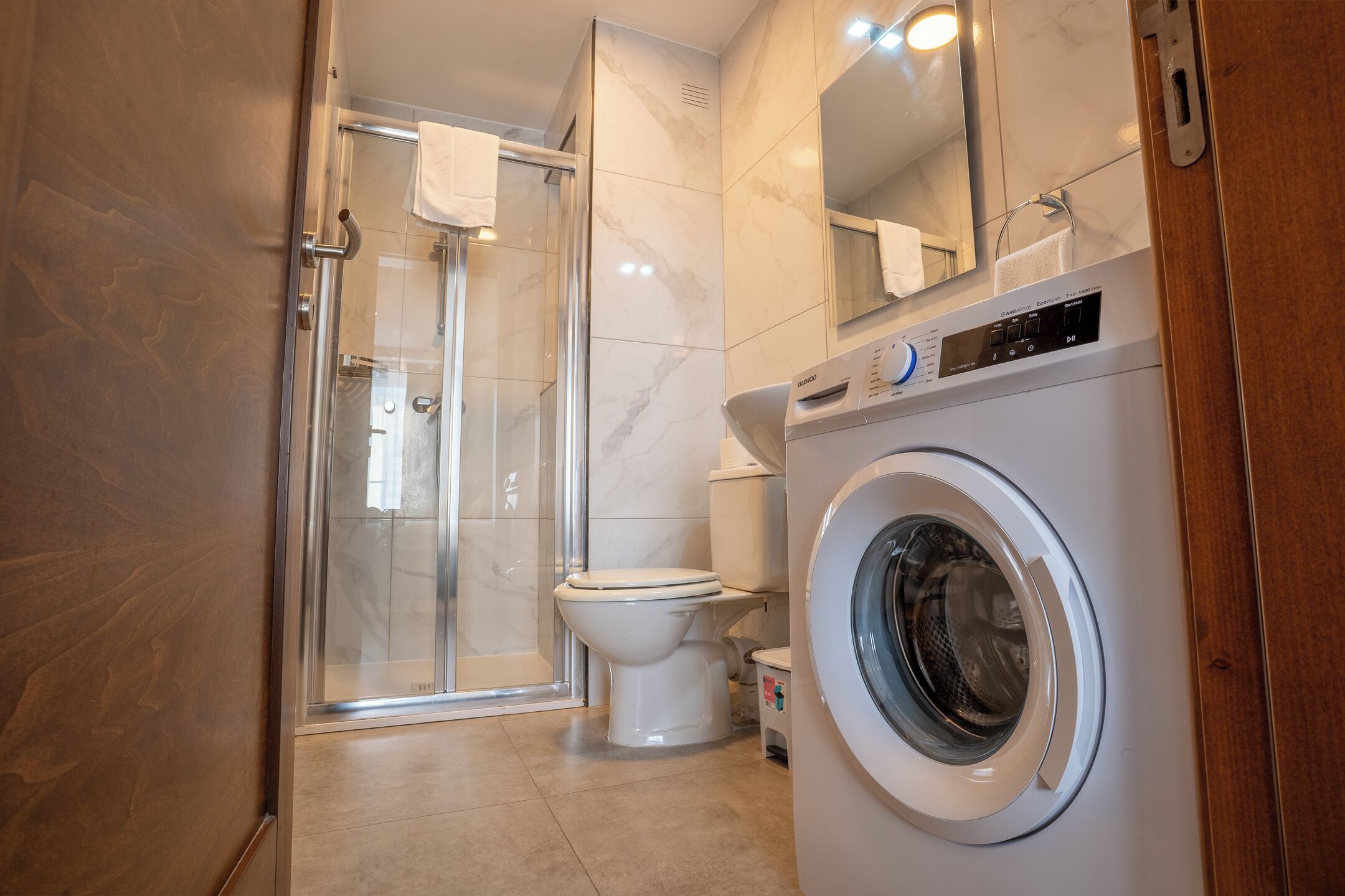 Ein Badezimmer mit Duschkabine aus Glas, Toilette und einer Waschmaschine mit Frontlader.