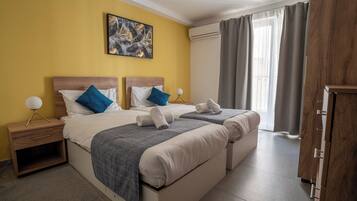 Habitación de hotel con dos camas, una mesita de noche con lámpara, un cuadro en la pared y vistas al exterior a través de la ventana.