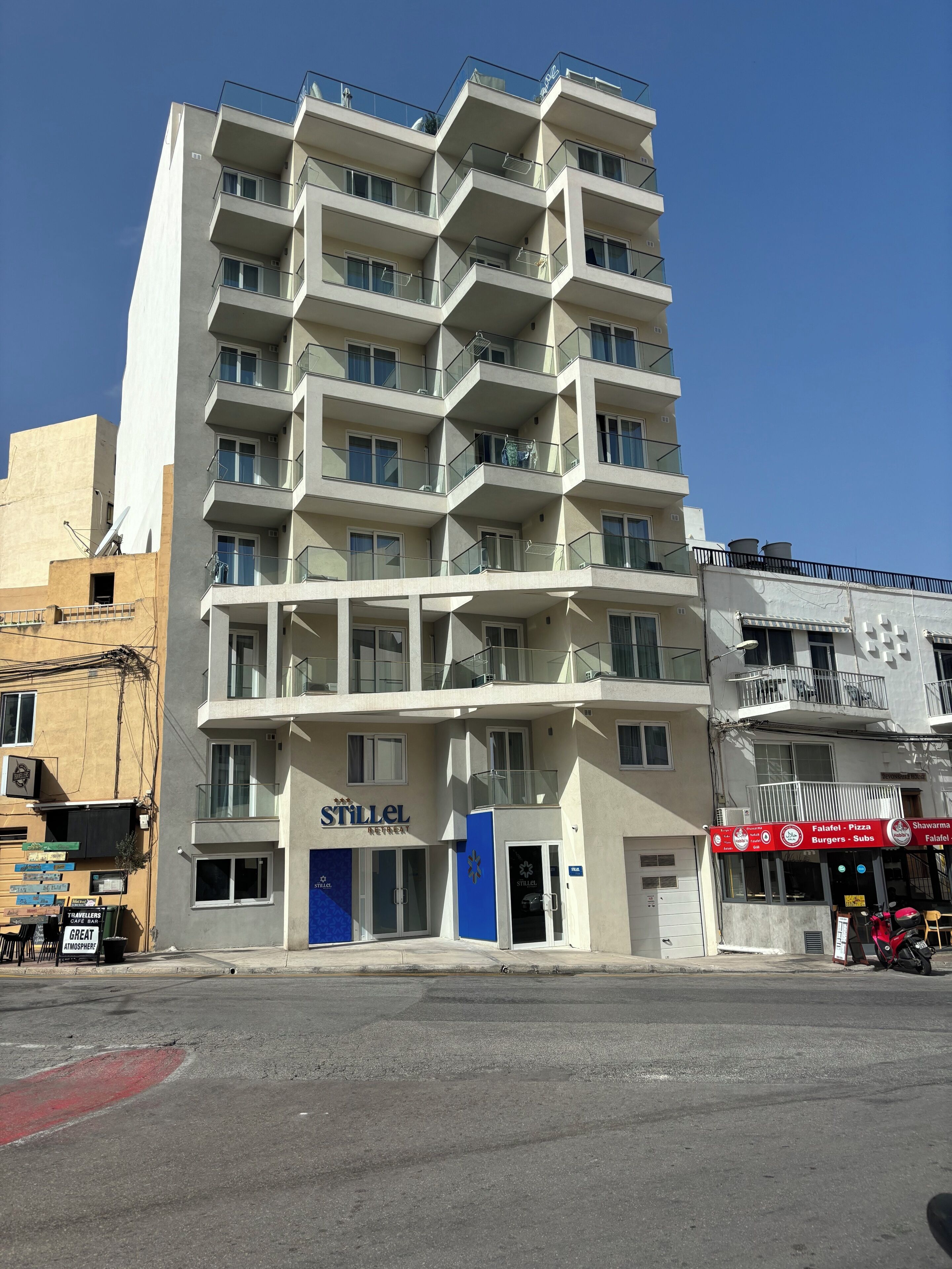 A multi-story hotel with a modern design, featuring balconies on each floor, a visible entrance, and a sign for a restaurant named "Stillel".