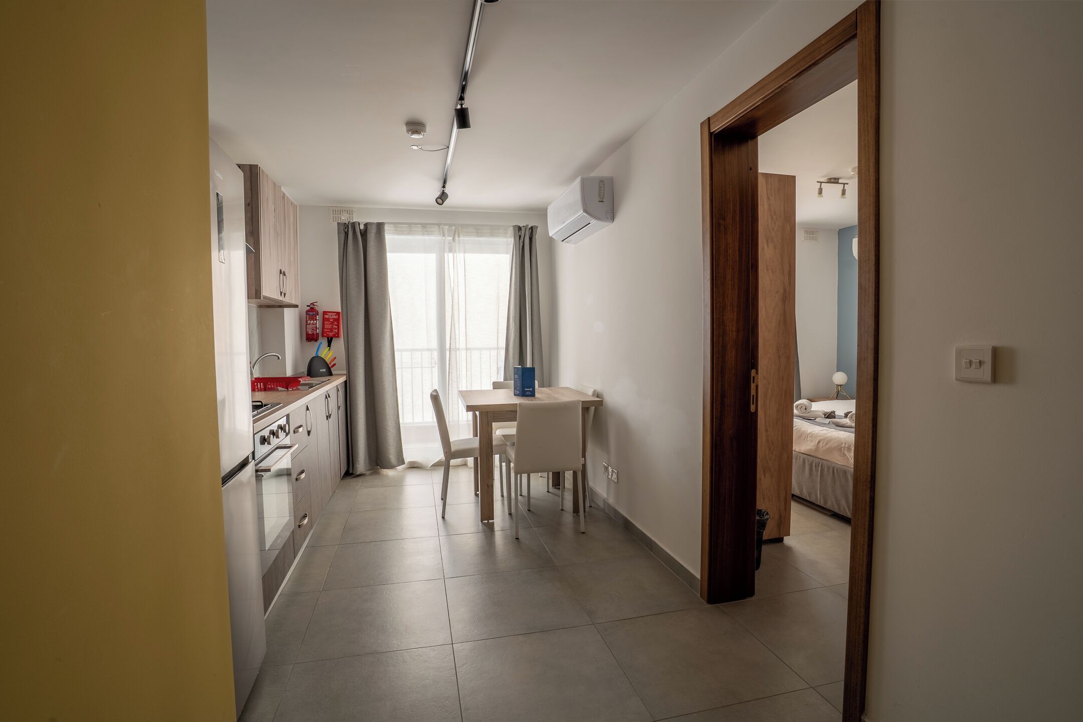 A compact kitchen with a dining area, a visible fire extinguisher, and a ceiling-mounted air conditioner.
