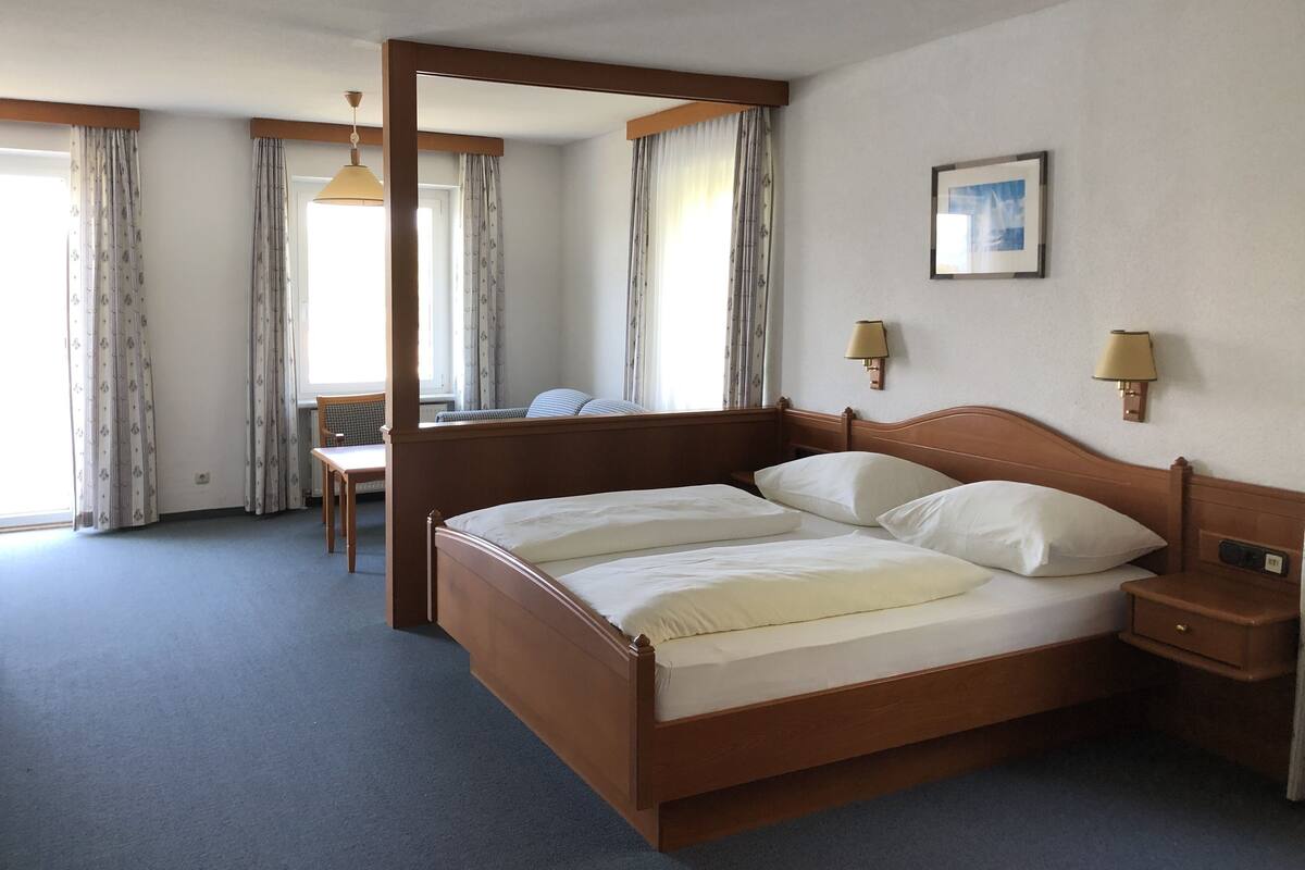 Una cama con dosel con estructura de madera, una mesita de noche con lámpara y un escritorio con silla en una habitación de hotel.