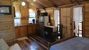 Un interno accogliente di una baita, con arredamento in legno, angolo cottura, un letto e zona pranzo.