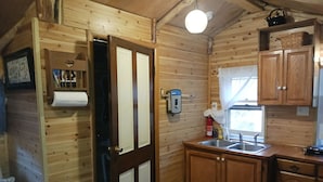 Interno di una baita in legno con angolo cottura, dotato di lavello, pensili e una finestra.