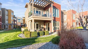 Un immeuble résidentiel moderne à deux étages, doté d’un balcon, d’un patio couvert et d’un jardin bien entretenu.