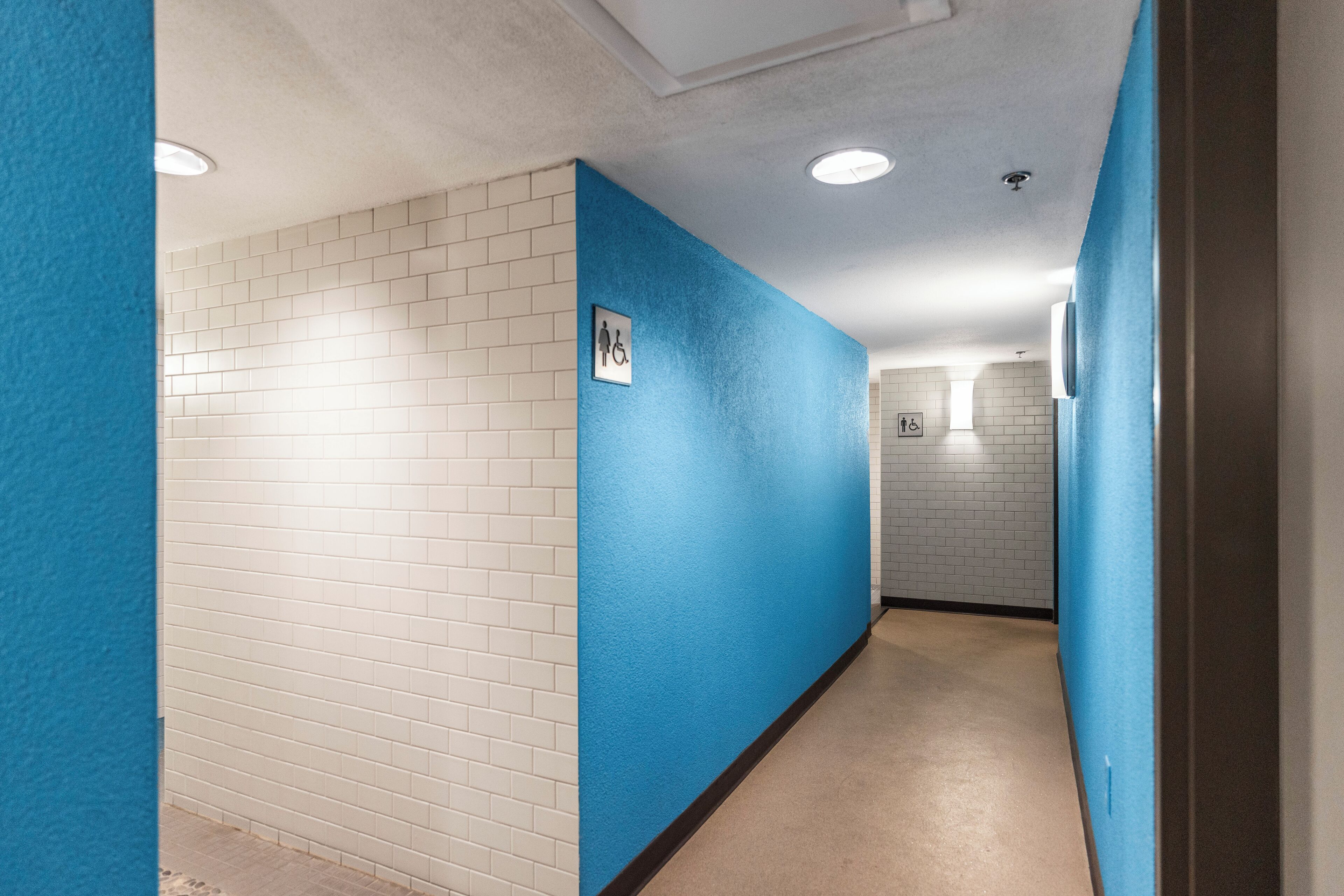 Un couloir aux murs en briques peintes en blanc et en bleu, avec un panneau indiquant qu’il est accessible aux personnes en fauteuil roulant.