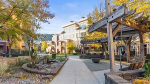 Un chemin piétonnier bordé de bancs et agrémenté d’une pergola, menant à un bâtiment doté de nombreuses fenêtres et d’une façade en pierre.