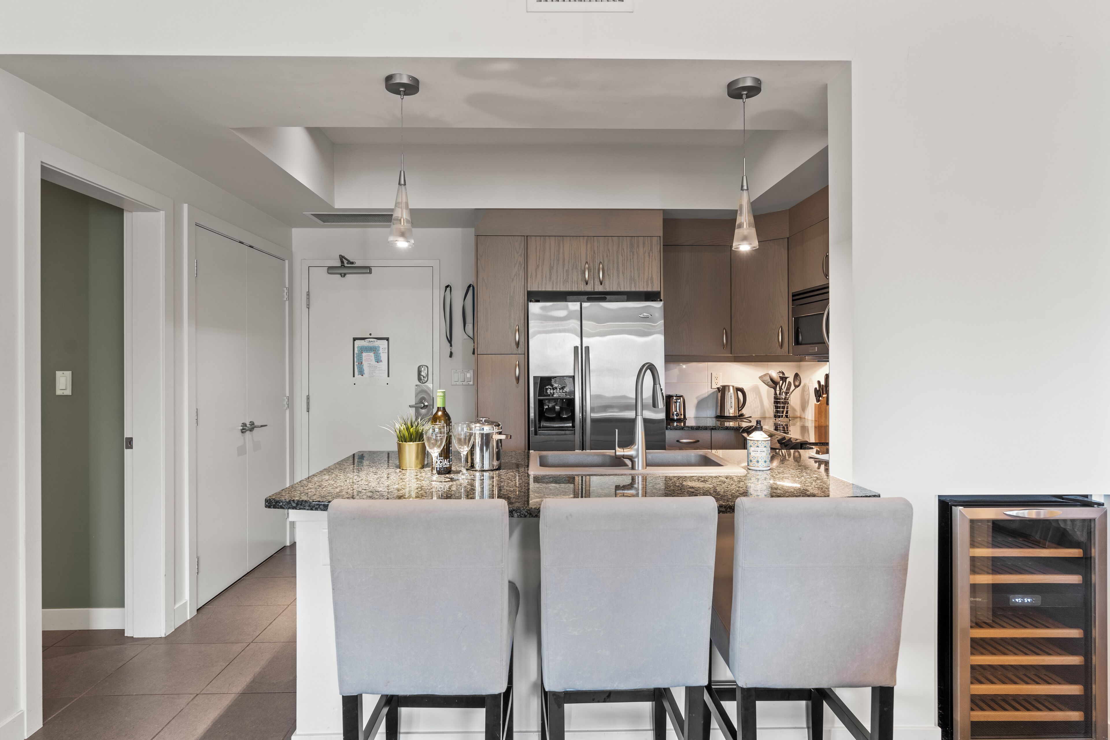 Une cuisine moderne dotée d’un îlot central, d’appareils électroménagers en acier inoxydable et de luminaires suspendus.
