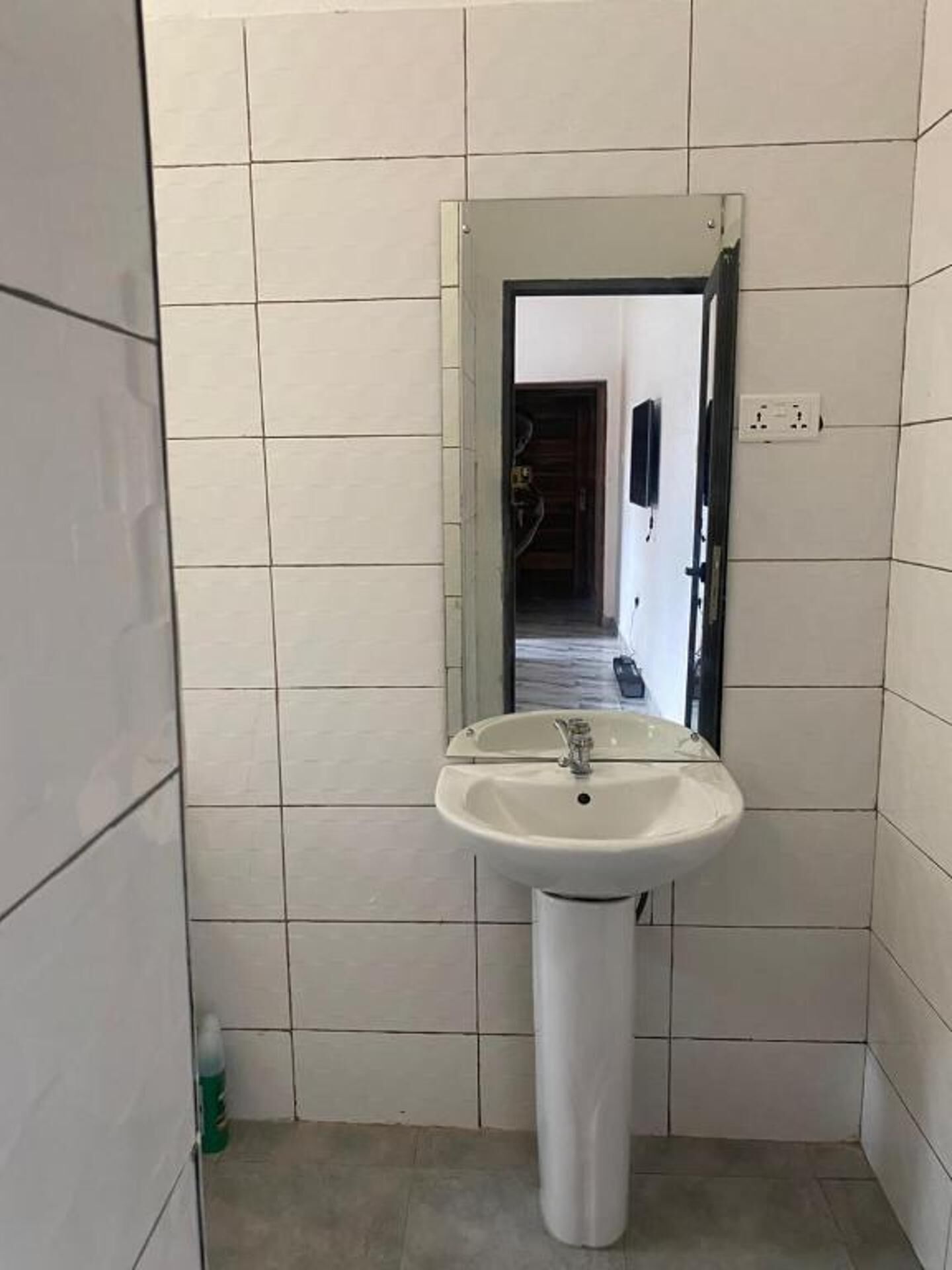 A bathroom with a white pedestal sink, tiled walls, and a visible electrical outlet.
