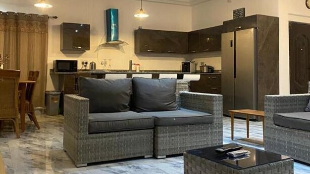 A modern living room with a sectional sofa, a coffee table, and a dining area with a table and chairs. - Sleep6-casa Blanca-privategarden-offstreet-kasoa (Kasoa)