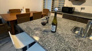 A kitchen with a granite countertop, a bottle of wine, a wine glass, and a microwave. - Sleep6-casa Blanca-privategarden-offstreet-kasoa (Kasoa)