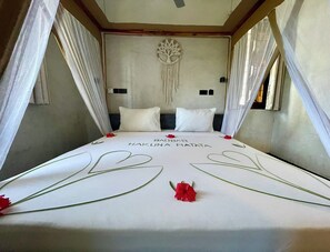 Ein Bett mit Baldachin, weißer Bettwäsche und einem Wandbehang aus Makramee.