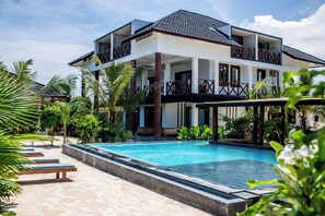 A two-story building with a swimming pool, surrounded by palm trees and lounge chairs. - Baobab Bungalows  (Jambiani)