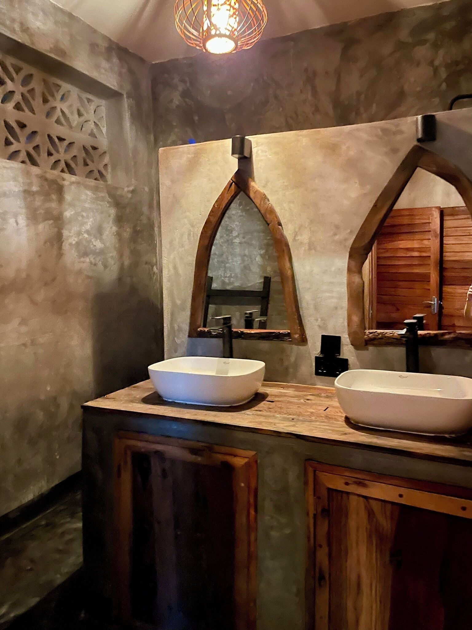 Une salle de bain au style rustique, dotée de deux vasques blanches, de meubles en bois et d’un miroir arqué original.