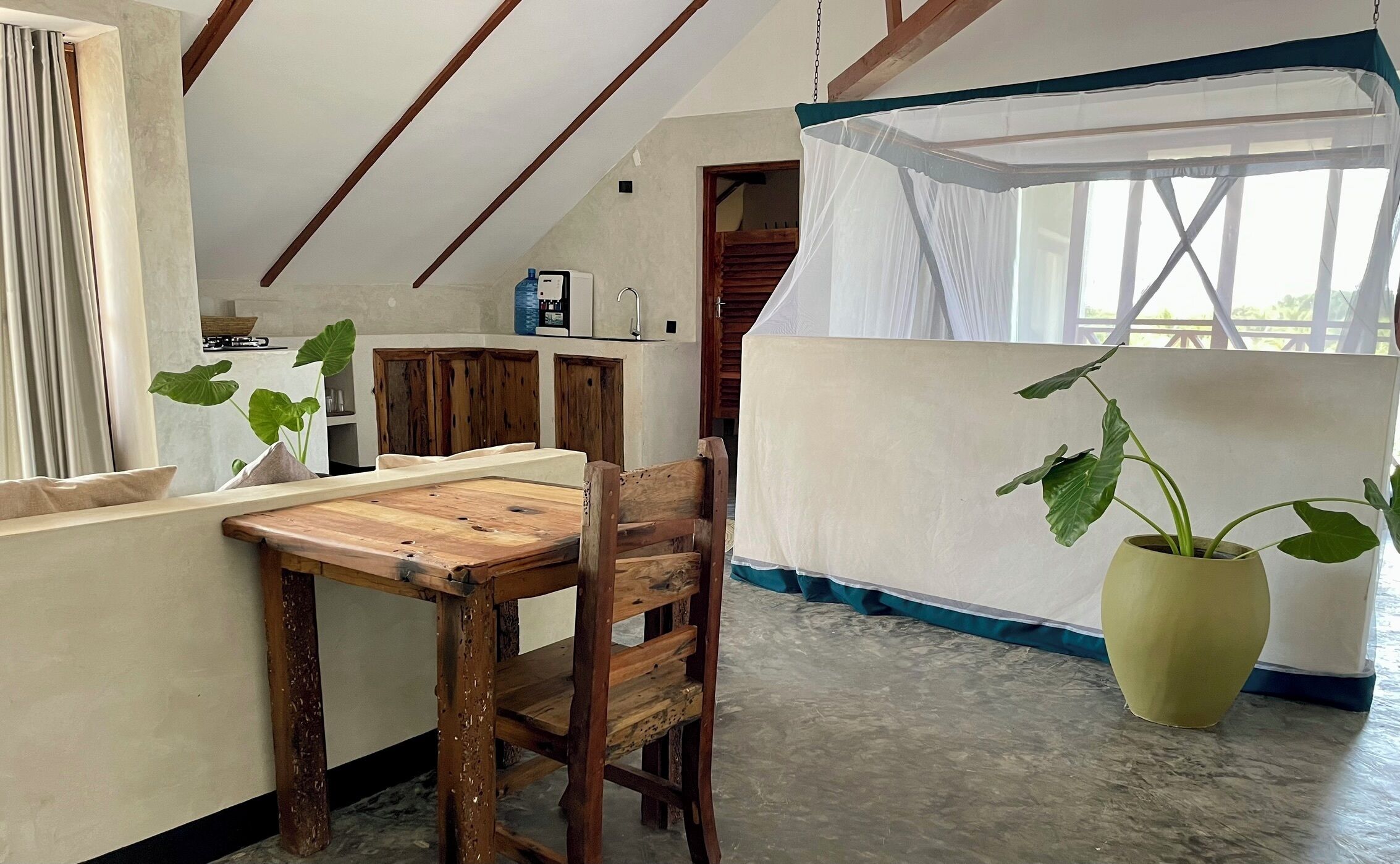 A rustic kitchen with wooden cabinets, a dining table, and a large potted plant.