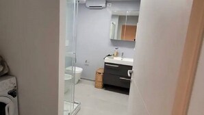 Une petite salle de bain dotée d’une douche à parois de verre, de toilettes et d’un meuble-lavabo avec un miroir.
