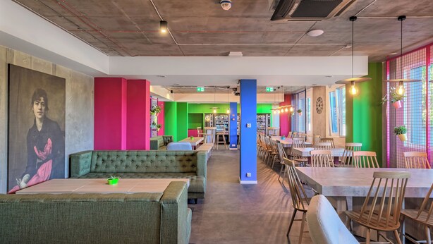 Une bibliothèque ou une salle de lecture moderne, dotée d’espaces de détente aux couleurs vertes et roses, de tables en bois et d’une grande bibliothèque.