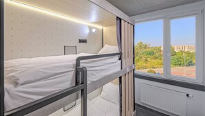 Une chambre avec un lit superposé, une fenêtre, des murs blancs et un radiateur.