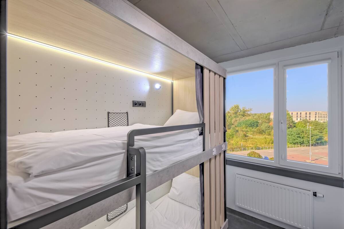 Ein Schlafraum mit Etagenbetten, einem Fenster, weißen Wänden und einer Heizung.
