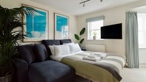 A modern hotel room with a sofa, a bed with a striped blanket, a flat-screen TV, and two framed artworks on the wall. - Colourful House 3 Bed Apt - Notting Hill (London)