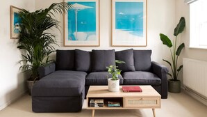 A modern living room with a dark grey sectional sofa, a wooden coffee table with books, and two large framed artworks on the wall. - Colourful House 3 Bed Apt - Notting Hill (London)