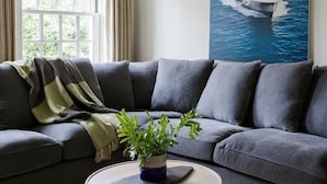 Ein modernes Wohnzimmer mit einem grauen Sofa, einem runden Couchtisch mit Pflanze und einem Gemälde einer Küstenlandschaft.