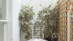 Een klein terras met een ronde tafel en twee stoelen, omringd door potplanten en een houten schutting met latten.