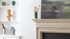 Een woonkamer met een open haard, een boekenkast en een schilderij.