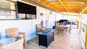 A covered outdoor patio with a glass-top table, chairs, and a grill area. - Charming & Rustic 4-bedroom Home with Hot Tub, Golf Cart, and large yard! (Dandridge)