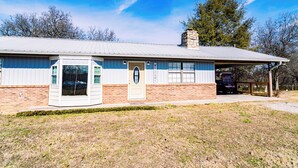 A single-story building with a brick base and a metal roof, featuring a front door and windows. - Charming & Rustic 4-bedroom Home with Hot Tub, Golf Cart, and large yard! (Dandridge)