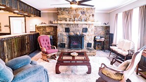A cozy living room with a stone fireplace, a ceiling fan, and comfortable seating. - Charming & Rustic 4-bedroom Home with Hot Tub, Golf Cart, and large yard! (Dandridge)