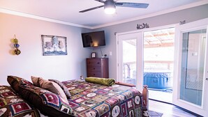 A bedroom with a bed, a dresser, a television, and a sliding glass door leading to an outdoor area. - Charming & Rustic 4-bedroom Home with Hot Tub, Golf Cart, and large yard! (Dandridge)