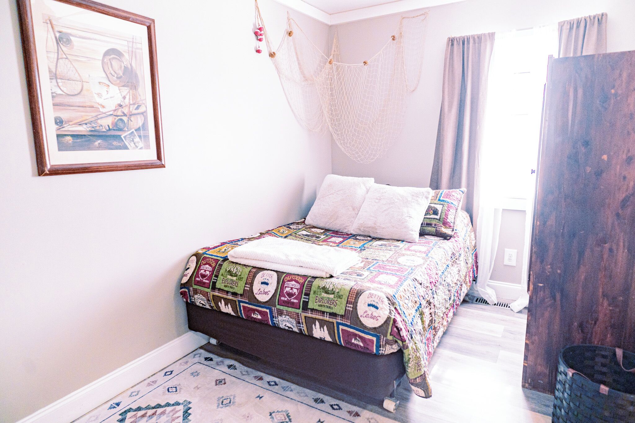 Una cama con un colcha colorida, una mosquitera colgante, un cuadro enmarcado y una puerta de madera.