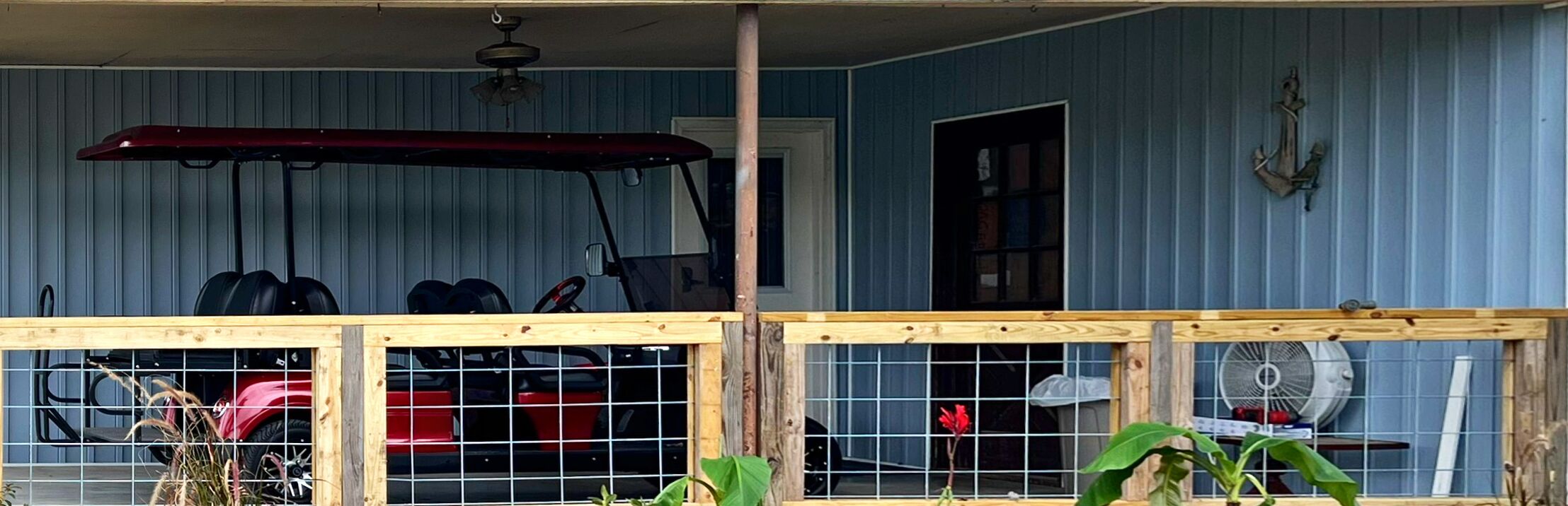A covered porch with a red vehicle, a fan, and a wooden railing.