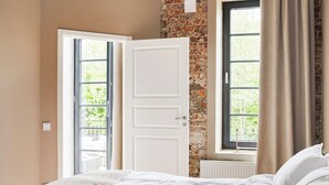A bedroom with a brick wall, a large window with curtains, a white door, and a bed with white bedding. - Mörrum River  (Mörrum)