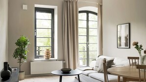 A modern living room with a sofa, dining table, and chairs. There is a large window with curtains, a radiator, and a potted plant. - Mörrum River  (Mörrum)