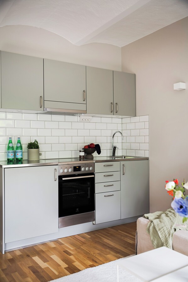Cocina compacta con armarios grises claros, horno de acero inoxidable y salpicadero de azulejos blancos.