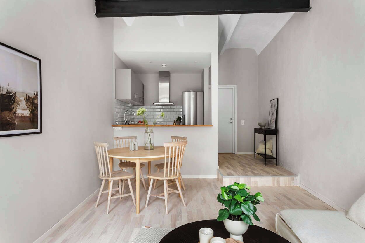 A modern living room with a dining area, a kitchen in the background, and a staircase leading to another level.