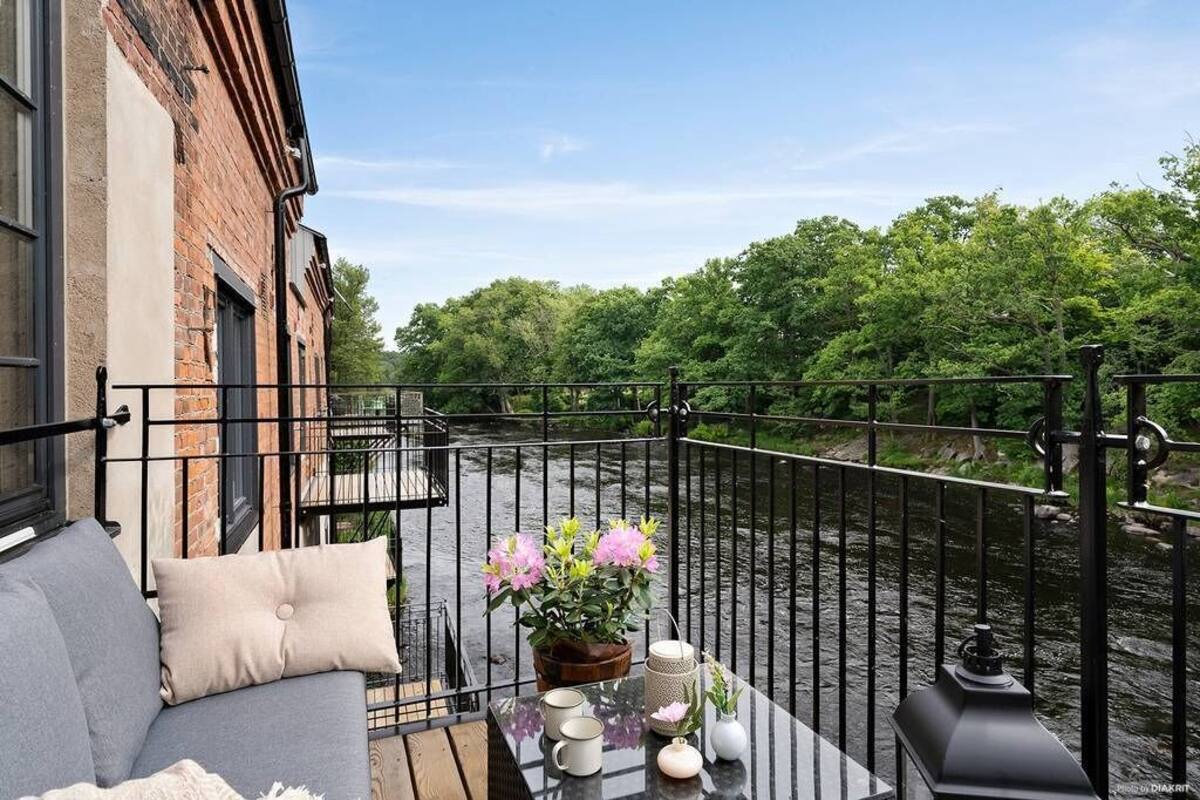 A balcony with a sofa, a table with decorative items, and a view of a river and trees.
