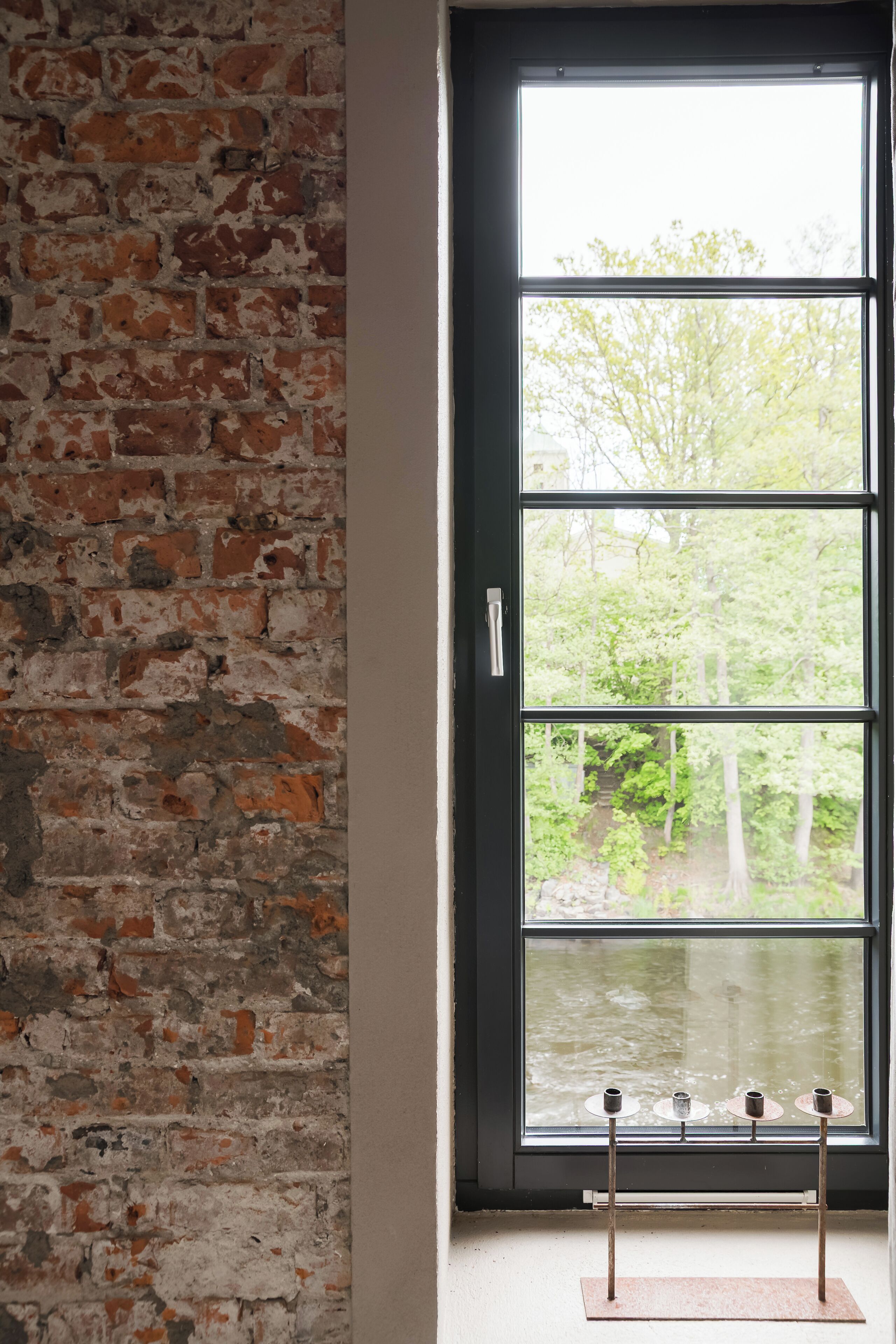 A room with a brick wall and a large window with three candle holders.