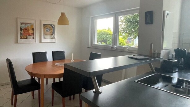 A modern kitchen with a dining area, featuring a large window, a built-in oven, and a dining table with chairs. - Beautiful vacation apartment "Karl May" in Elspe/Sauerland, approx. 65 sqm, for 1-4 persons (Lennestadt)