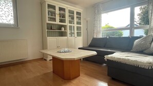 A living room with a wooden coffee table, a grey sofa, a white cabinet with glass doors, and a window with curtains. - Beautiful vacation apartment "Karl May" in Elspe/Sauerland, approx. 65 sqm, for 1-4 persons (Lennestadt)