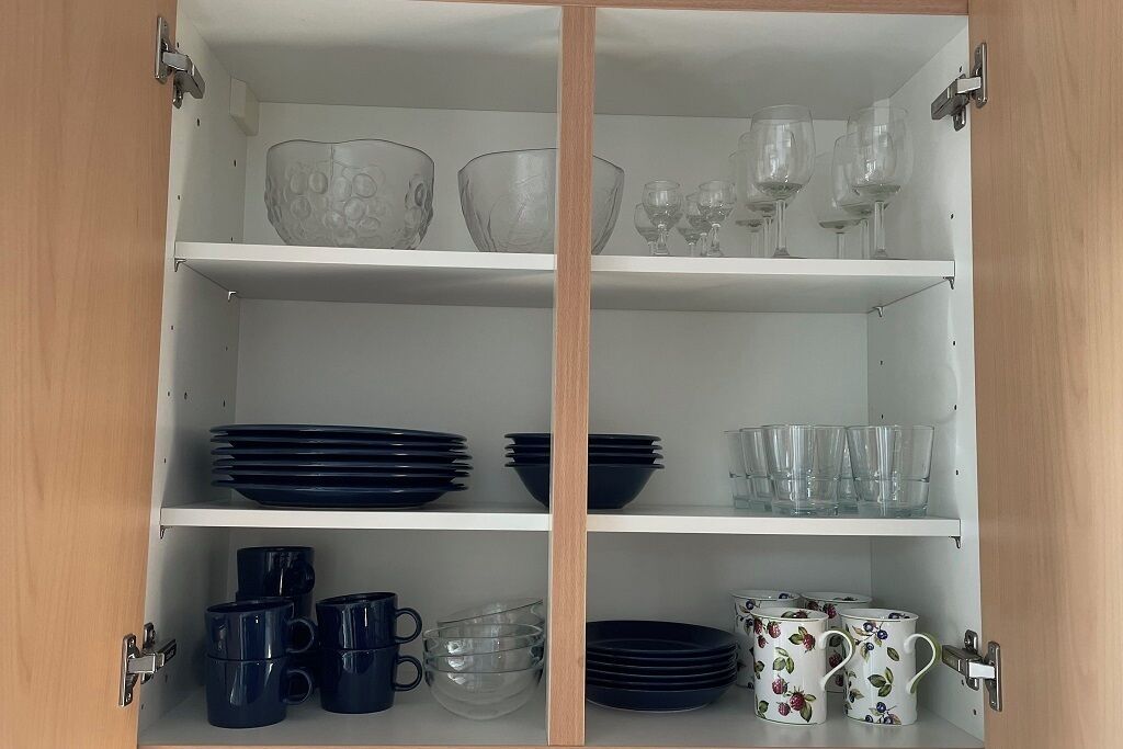 A white cabinet with three shelves, each holding various glassware and dishes.