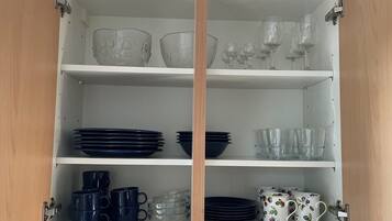 A white cabinet with three shelves, each holding various glassware and dishes.