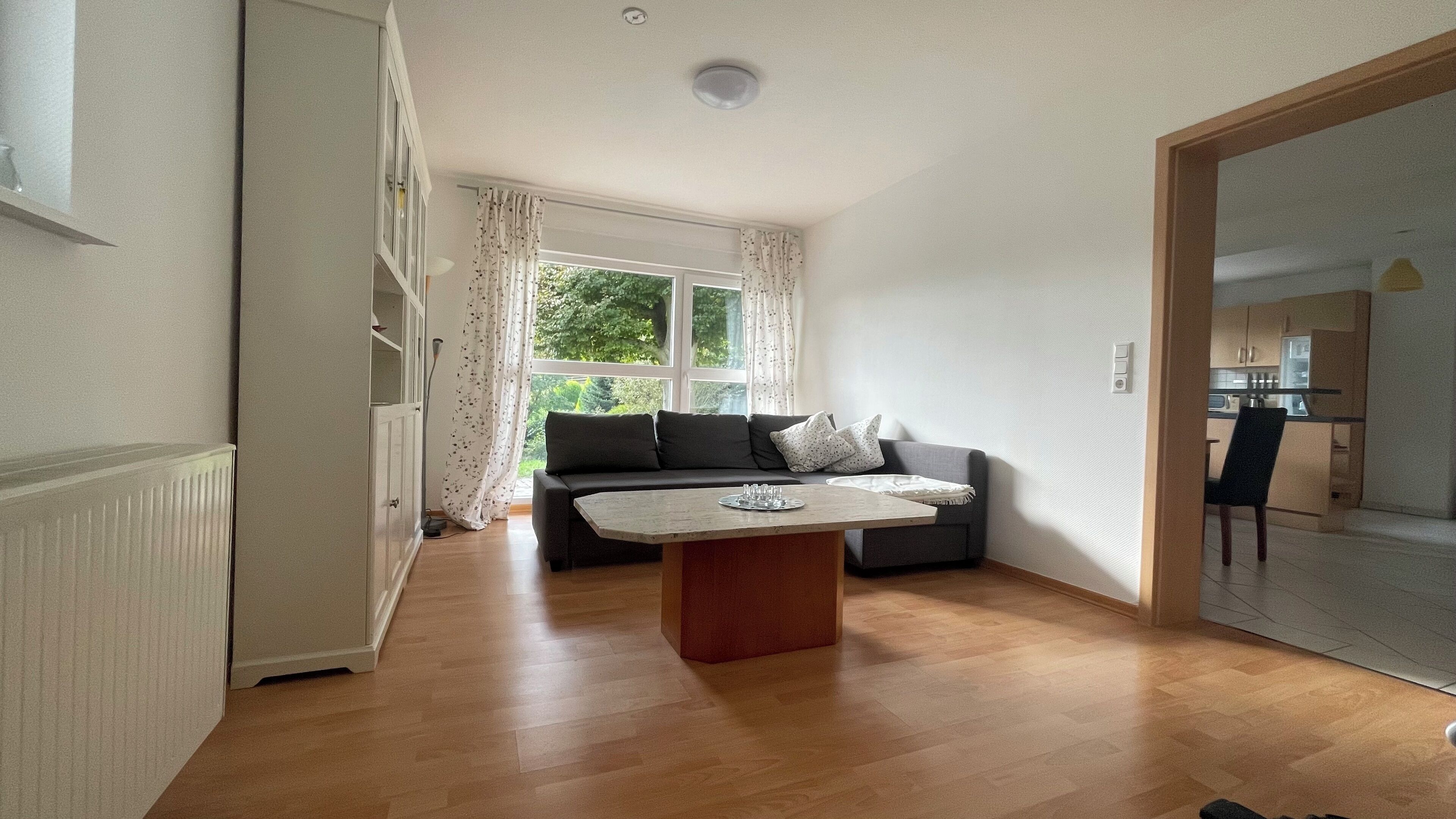 Ein modernes Wohnzimmer mit einer Couch, einem Couchtisch und Blick auf eine Küche durch eine offene Tür.