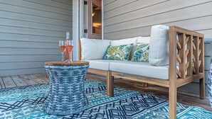 A white sofa with colorful cushions, a woven side table, and a patterned rug on a wooden deck. - 4005 Rookery 3 Sea Story With 2 Pools Beach Access and Lots of Beach Amenities (Gulf Shores)