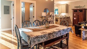 A dining area with a table set for four, surrounded by chairs. A chandelier hangs above, and a cabinet with a shark decoration is visible in the background. - 4005 Rookery 3 Sea Story With 2 Pools Beach Access and Lots of Beach Amenities (Gulf Shores)