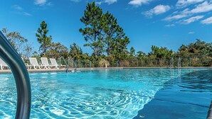 A clear blue pool with white lounge chairs and metal railings, surrounded by trees and a clear sky. - 4005 Rookery 3 Sea Story With 2 Pools Beach Access and Lots of Beach Amenities (Gulf Shores)