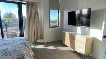Un dormitorio moderno con una cama grande, un televisor montado en la pared y vistas al exterior a través de una ventana.